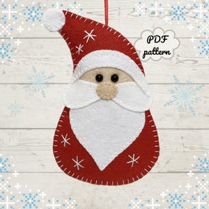 Könnte beinhalten: Ein rot-weißes Filz-Weihnachtsornament in Form eines Weihnachtsmanns mit einem genähten Design. Das Ornament hat einen weißen Bart, eine beige Nase und schwarze Augen. Der Text "PDF pattern" befindet sich in einer Sprechblase.