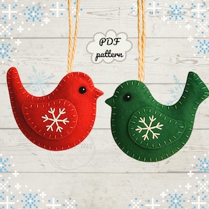 May include: Two felt bird ornaments, one red and one green, each with a white snowflake applique. They hang from tan string against a white wood background with a snowflake pattern. The text "PDF pattern" is in a cloud.