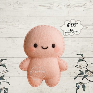 Könnte beinhalten: Eine hellrosa Filzpuppe mit einem lächelnden Gesicht, rosigen Wangen und gestickten Details. Die Puppe hat einen runden Kopf, Arme und Beine. Die Worte "PDF pattern" stehen in einer wolkenförmigen Grafik. Das ColorPins-Logo ist sichtbar.
