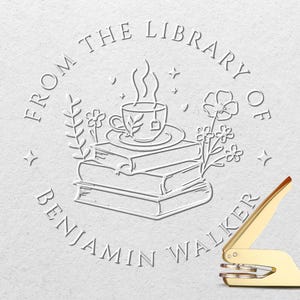 May include: A gold-colored embosser with a red handle, next to a white embossed design. The design features a teacup on a stack of books, surrounded by floral elements and the text "FROM THE LIBRARY OF BENJAMIN WALKER."