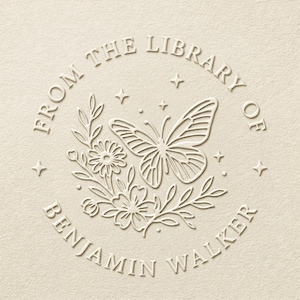 Peut inclure: Motif en relief de couleur crème avec un papillon, des fleurs et le texte "FROM THE LIBRARY OF BENJAMIN WALKER". Le motif est circulaire, avec le texte en arc de cercle en haut et en bas. Quatre petites étoiles sont espacées.