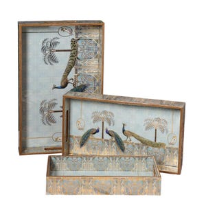 Könnte beinhalten: Set aus drei dekorativen Holztabletts. Die Tabletts haben einen hellblauen Hintergrund mit Pfauen- und Palmenmotiven. Sie haben eine rechteckige Form mit Holzrahmen und Griffen.