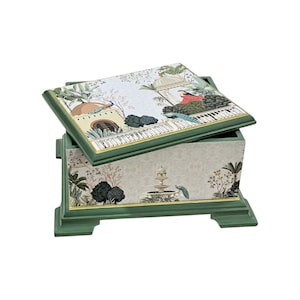 Puede incluir: Una caja rectangular de madera con marco verde salvia y borde dorado. La tapa y los laterales presentan una escena de jardín impresa con una fuente, árboles frondosos y pavos reales. La caja tiene una tapa extraíble y cuatro patas.