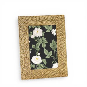 May include: A rectangular gold-colored picture frame with a textured surface. The frame holds a floral print with white roses and green leaves on a black background. The frame is designed to hold a 5x7 inch photo.