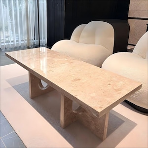 Pode incluir: Uma mesa de centro retangular de mármore claro com uma superfície polida. A mesa tem duas pernas de suporte com um design de recorte circular. A mesa tem aproximadamente 152 cm de comprimento e 51 cm de largura.