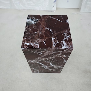 May include: A hexagonal side table with a rich, dark red marble top and sides, featuring striking white veining. The table's geometric design adds a modern touch to any space. The table is approximately 20 inches tall.