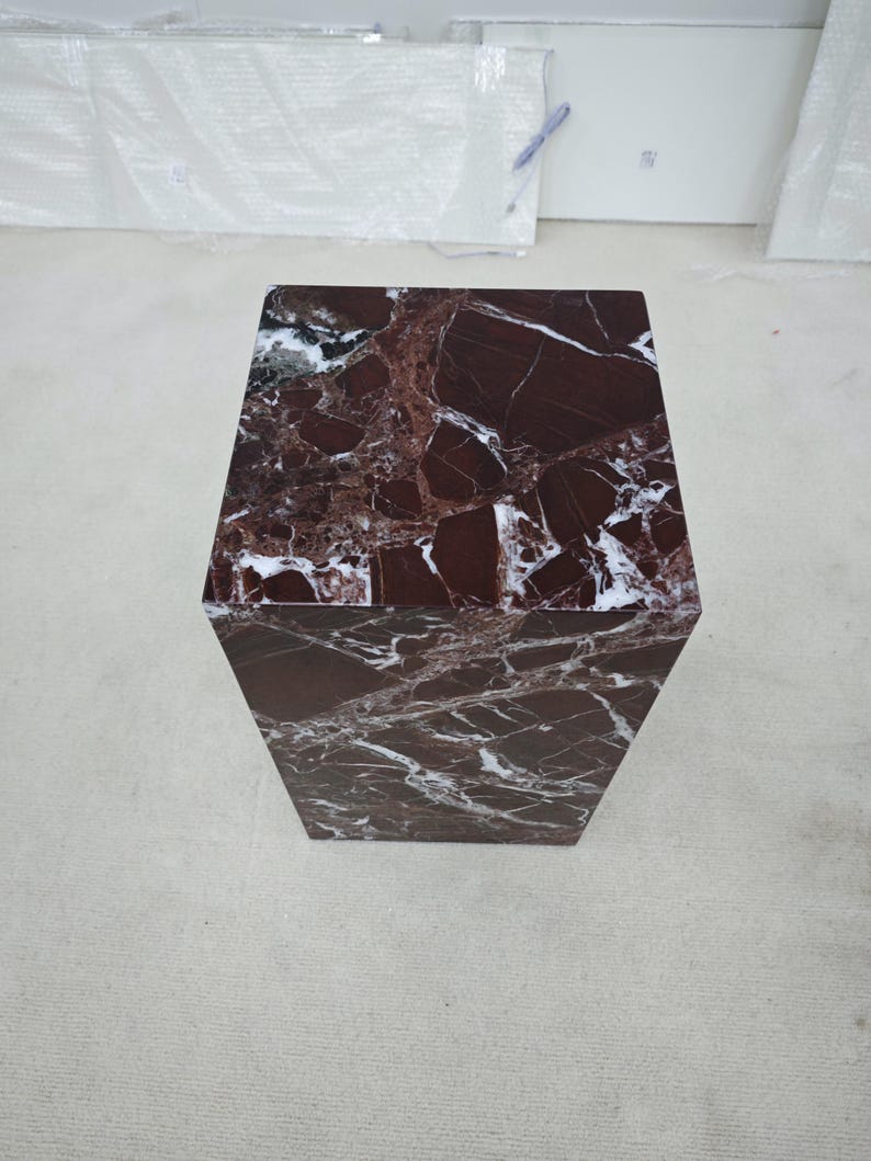May include: A hexagonal side table with a rich, dark red marble top and sides, featuring striking white veining. The table's geometric design adds a modern touch to any space. The table is approximately 20 inches tall.