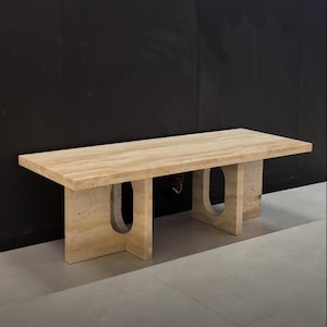 Puede incluir: Mesa rectangular de piedra beige con diseño minimalista. La mesa tiene una parte superior plana y dos bases de soporte, cada una con un gran recorte ovalado. La mesa mide aproximadamente 183 cm de largo.