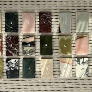 Könnte beinhalten: Eine Sammlung von einundzwanzig rechteckigen Steinplatten, jede mit einem einzigartigen Muster und Farbe. Die Fliesen variieren in den Farbtönen Weiß, Grün, Rosa, Rot und Braun. Die Fliesen sind in Reihen und Spalten angeordnet.