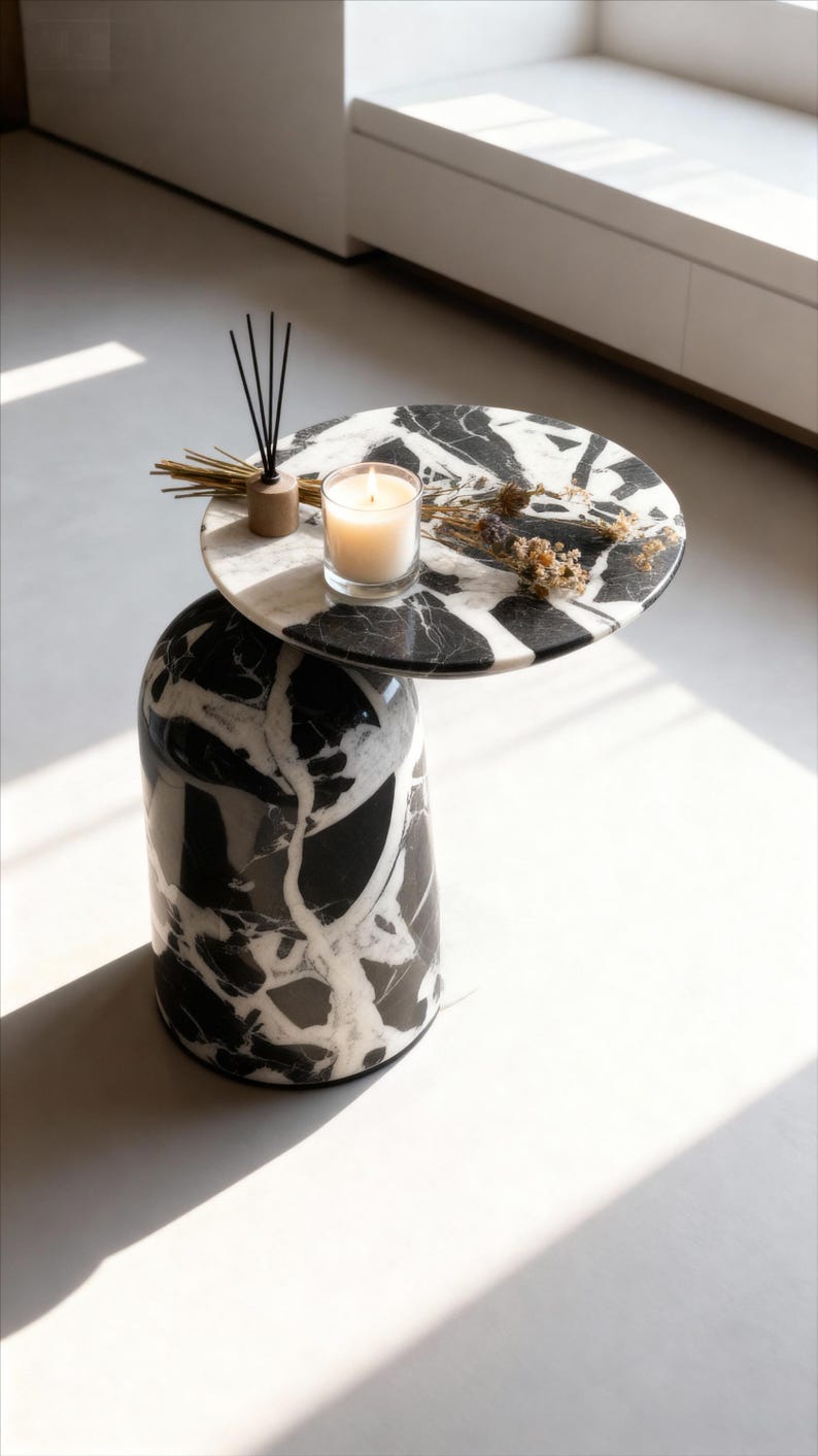 Puede incluir: Una mesa auxiliar moderna con base cil&iacute;ndrica y tapa redonda, ambas con un patr&oacute;n de m&aacute;rmol blanco y negro. Una vela encendida, flores secas y un difusor de ca&ntilde;a se encuentran sobre la mesa.