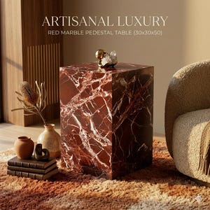 May include: A red marble pedestal table with white veining, measuring approximately 12x12x20 inches. The table is a cube shape and has a decorative gold object and crystal on top. The text "ARTISANAL LUXURY" is at the top of the image.