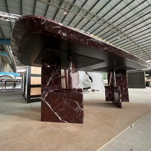 May include: A large, rectangular table with a dark burgundy marble top and black supports. The marble has white veining. The table is supported by four rectangular legs. The table is likely for a dining room or conference room.