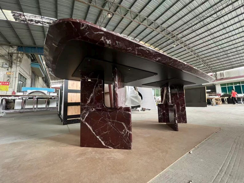 May include: A large, rectangular table with a dark burgundy marble top and black supports. The marble has white veining. The table is supported by four rectangular legs. The table is likely for a dining room or conference room.