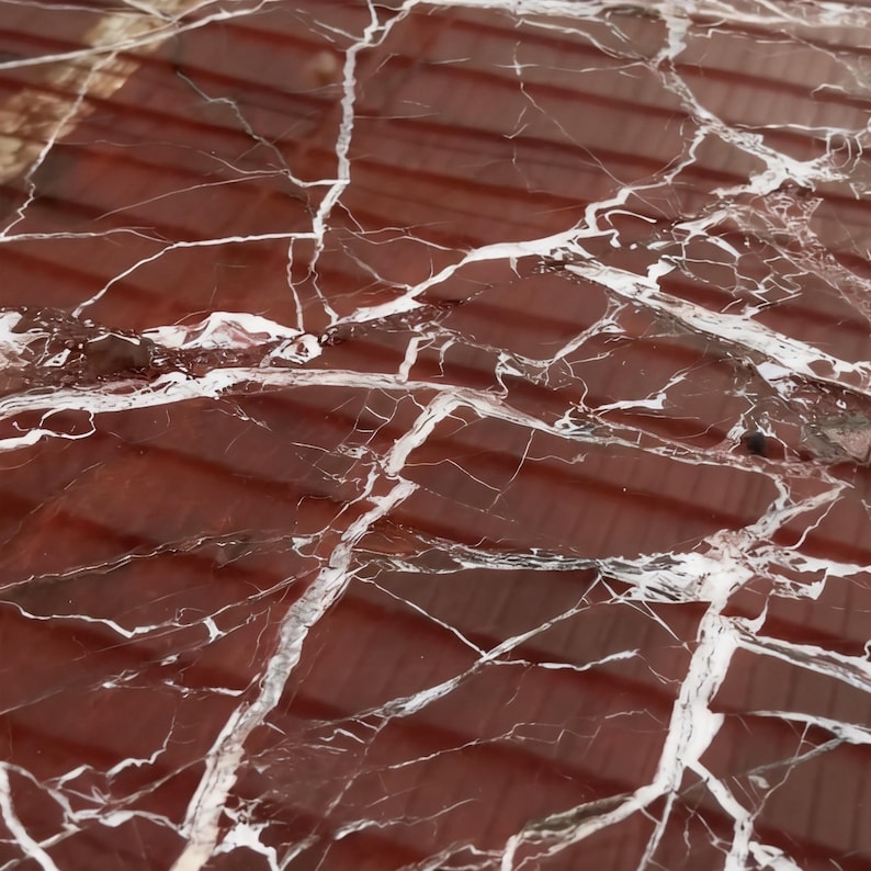May include: Close-up of a polished red marble surface with prominent white veining. The natural stone features a rich, deep red color with contrasting white streaks, creating a striking visual texture. The surface is smooth and reflective.