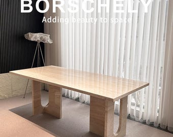 Może przedstawiać: Prostokątny stół z beżowego marmuru z nogami w kształcie litery U. Stół stoi przed oknem z białymi zasłonami. Tekst "BORSCHELY Adding beauty to space" znajduje się u góry obrazu.