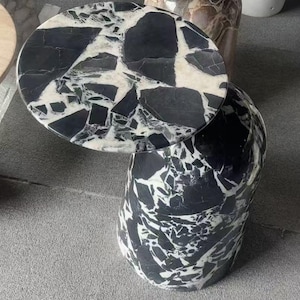Puede incluir: Una mesa auxiliar redonda con dise&ntilde;o de m&aacute;rmol blanco y negro. La tapa circular descansa sobre una base cil&iacute;ndrica. El patr&oacute;n de m&aacute;rmol presenta formas y vetas irregulares, creando un aspecto &uacute;nico y elegante.