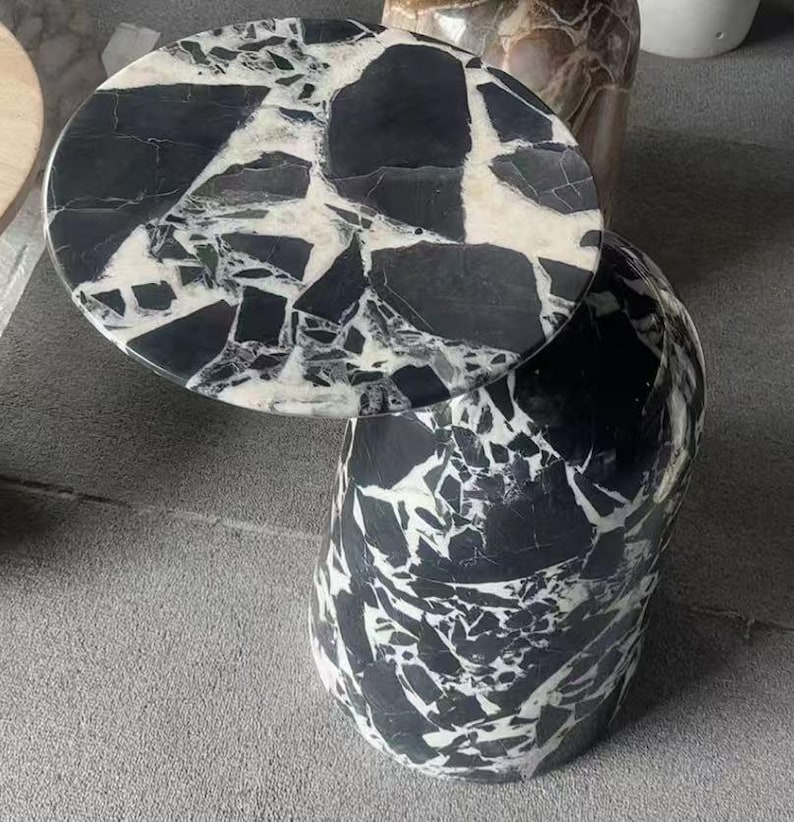 Puede incluir: Una mesa auxiliar redonda con dise&ntilde;o de m&aacute;rmol blanco y negro. La tapa circular descansa sobre una base cil&iacute;ndrica. El patr&oacute;n de m&aacute;rmol presenta formas y vetas irregulares, creando un aspecto &uacute;nico y elegante.