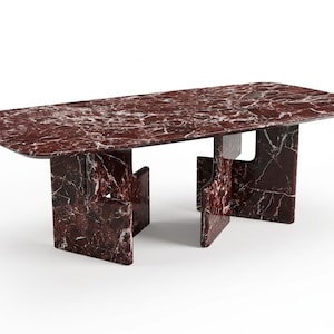 May include: A rectangular dining table with a red marble top and matching base. The table has rounded corners and a unique leg design. The marble features white veining throughout.