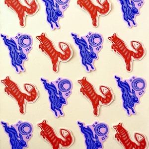 Puede incluir: Patr&oacute;n de pegatinas con zorros rojos y conejos azules con un dise&ntilde;o de luna creciente y estrellas. Las pegatinas tienen un borde blanco y est&aacute;n dispuestas sobre un fondo beige claro. Los dise&ntilde;os de zorro y conejo son estilizados.