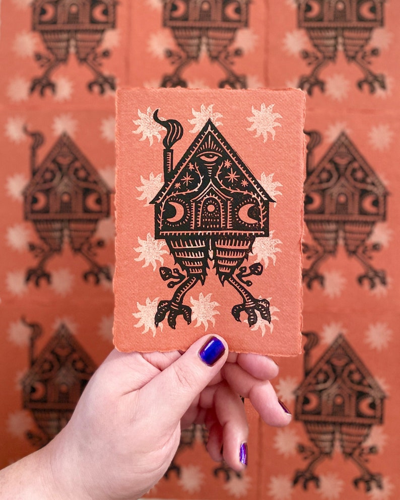 May include: A black and white print of a house with legs and a chimney on a peach colored background. The house has a single eye and is surrounded by white stars.