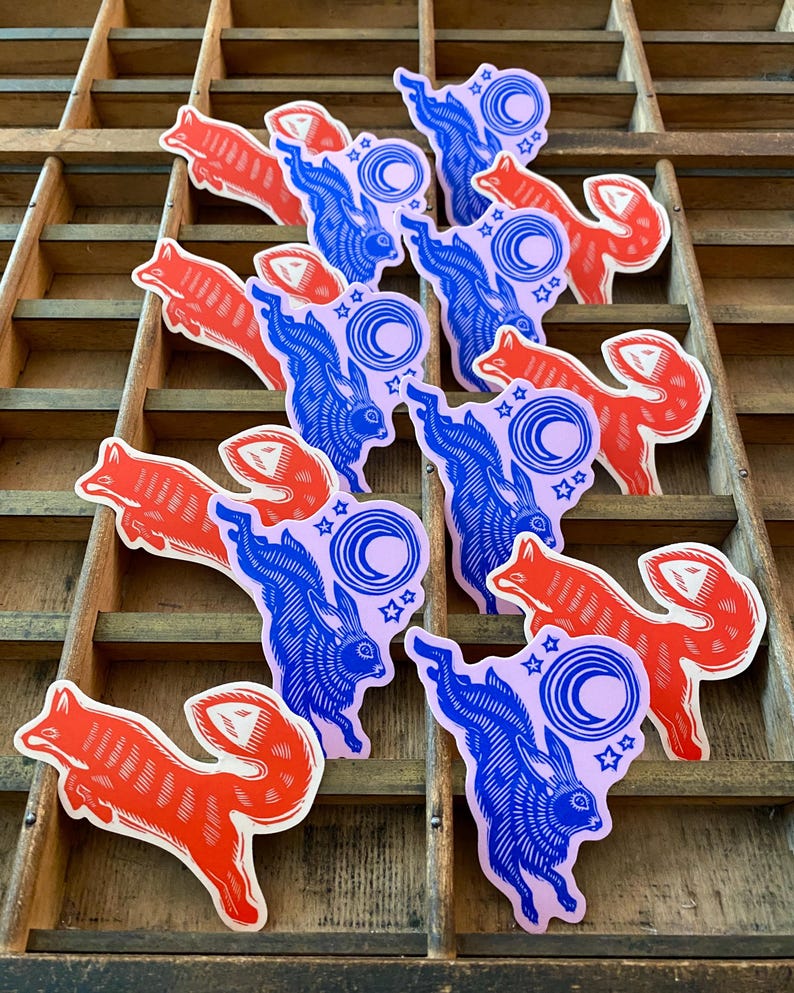 Puede incluir: Colecci&oacute;n de pegatinas con un zorro rojo y un conejo azul con un dise&ntilde;o de luna creciente y estrellas. Las pegatinas est&aacute;n dispuestas sobre una superficie de madera con m&uacute;ltiples compartimentos.
