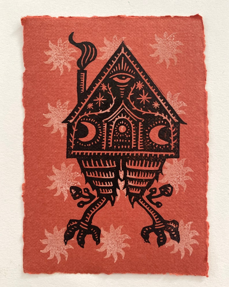 May include: A black and white linocut print of a house with a single eye, two moons, and stars. The house is on legs with claws and is surrounded by white sun-like shapes on a red background.