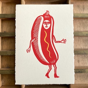 Puede incluir: Una impresión rectangular en papel color hueso que presenta una ilustración en linóleo rojo de un personaje de perrito caliente con rostro humano, brazos y piernas. El perrito caliente tiene una línea amarilla ondulada y lleva botas rojas.
