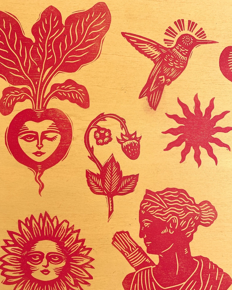 May include: Red linocut print on a yellow background featuring various botanical and celestial elements. Includes a radish with a face, a hummingbird, a sun, a strawberry plant, a sunflower, and a woman with a bundle.