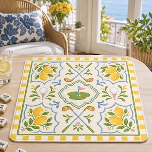 May include: A rectangular placemat with a golf theme. The off-white mat features a central green golf course design with a pink flag, surrounded by golf clubs, golf balls, and lemons. The border is yellow and green.