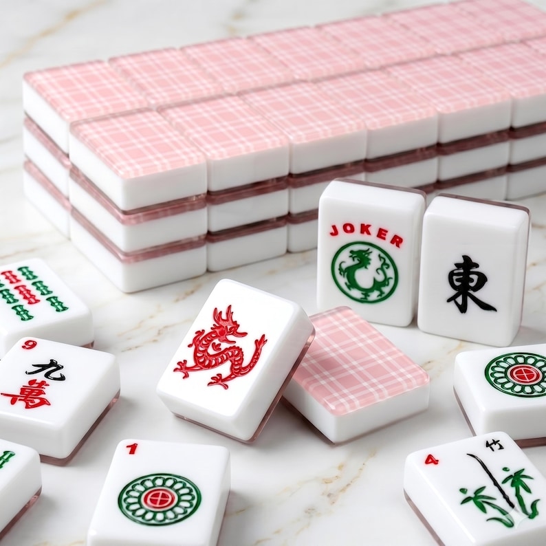 May include: A collection of white and pink Mahjong tiles, displaying diverse symbols and characters. The tiles are arranged in stacks and scattered, highlighting the game's elements. The tiles feature red, green, and black designs, including a dragon, a joker, and Chinese characters.