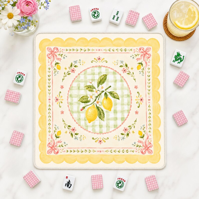 Pode incluir: Um tapete de Mahjong quadrado, creme, com uma borda amarela ondulada e um design central com lim&otilde;es, flores e um padr&atilde;o xadrez verde. La&ccedil;os rosa e detalhes florais adornam os cantos. Pe&ccedil;as de Mahjong e um copo de limonada s&atilde;o dispostos ao redor do tapete.