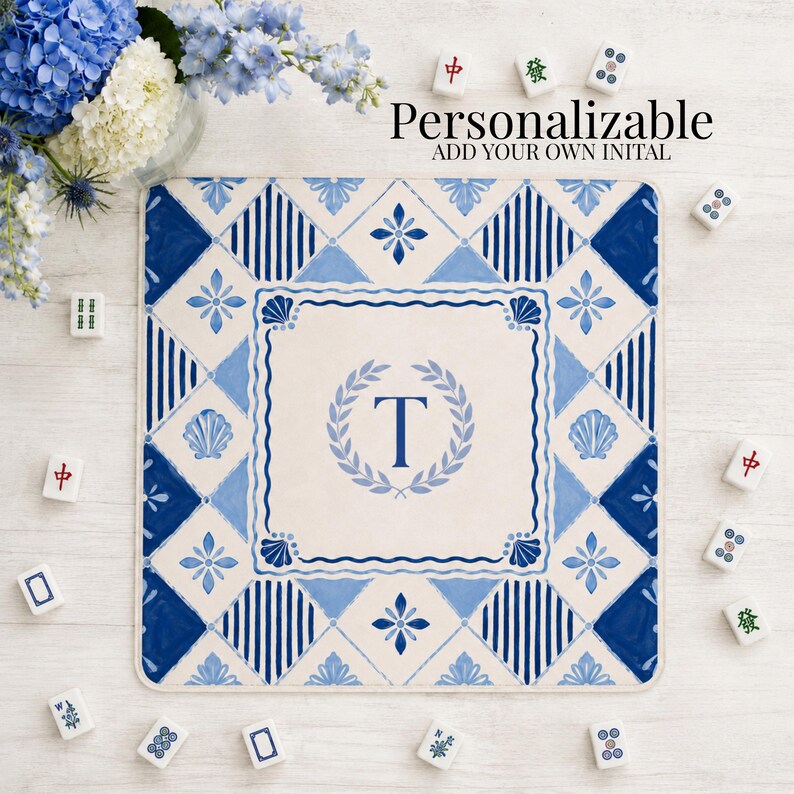 Op de afbeelding: Een vierkante, gepersonaliseerde mat met een blauw en wit tegelontwerp. De mat heeft een centraal monogram met de letter "T" in een lauwerkrans. De woorden "Personalizable" en "ADD YOUR OWN INITIAL" staan bovenaan.