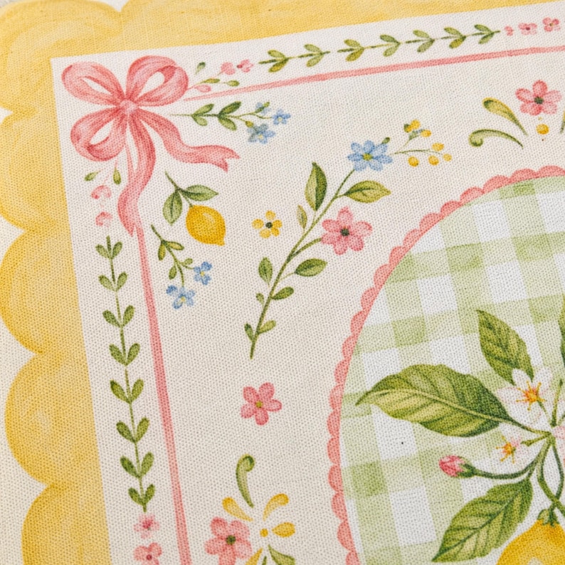 Pode incluir: Close-up de um tecido decorativo com um design de lim&atilde;o e floral. O tecido apresenta uma borda amarela ondulada, um la&ccedil;o rosa e um padr&atilde;o xadrez verde e branco. O design inclui lim&otilde;es, flores e folhas.