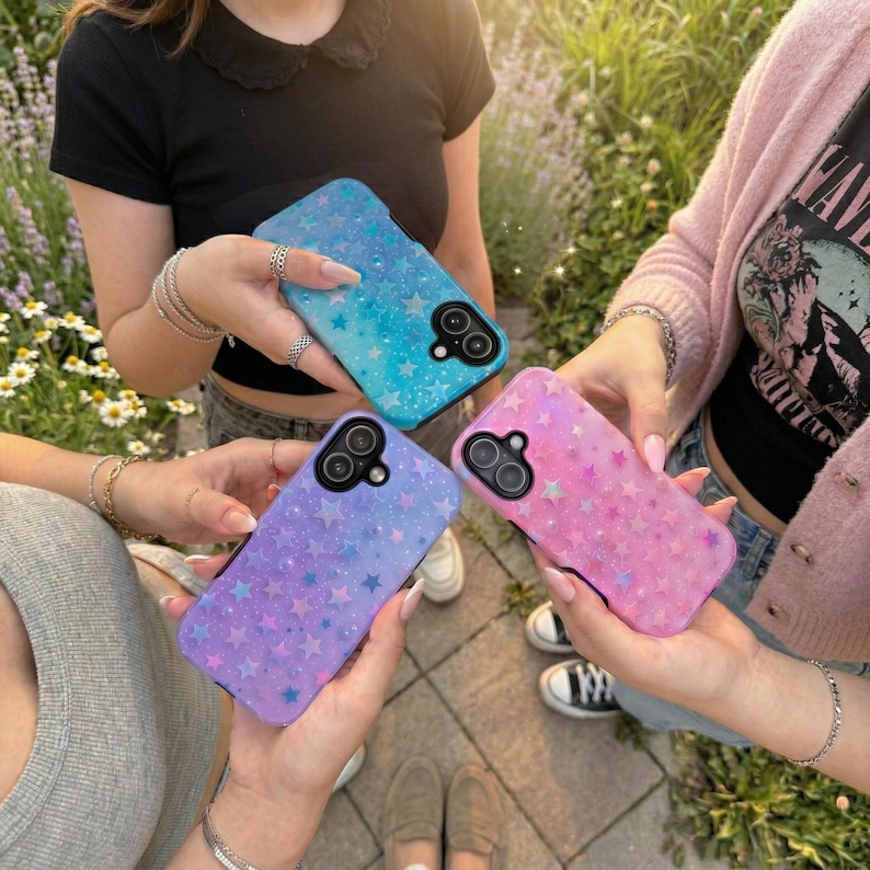 May include: Three phone cases in shades of blue, purple, and pink, each adorned with a star pattern. The cases are held by people, showcasing the colorful designs. The cases have a glossy finish and are designed for a smartphone.