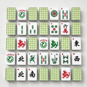 May include: A complete Mahjong set with white tiles featuring various symbols, numbers, and Chinese characters. The set includes green and white checkered tile racks. The tiles display dragons, circles, bamboo, and the word "Joker".