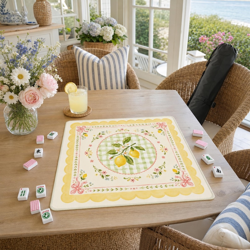 Pode incluir: Uma mesa de madeira montada para um jogo de Mahjong. No centro, um tapete decorativo com um desenho de lim&atilde;o. O tapete tem uma borda amarela com vieiras e um c&iacute;rculo quadriculado verde e branco com um ramo de lim&atilde;o. Pe&ccedil;as de Mahjong est&atilde;o espalhadas.