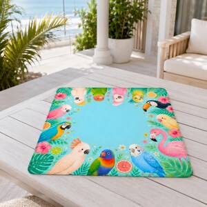May include: A rectangular mat with a vibrant tropical bird design. The mat features a light blue center surrounded by colorful parrots, flamingos, and tropical flowers. The mat is placed on a light-colored wooden table.