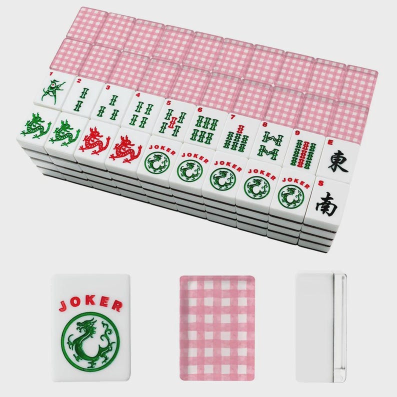 May include: A complete Mahjong set with white tiles featuring green and red dragon designs, along with the word "JOKER" and Chinese characters. The set includes pink patterned card-like pieces. The tiles are stacked neatly.