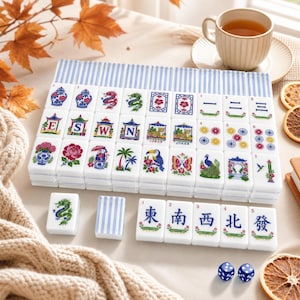 May include: A set of white mahjong tiles featuring colorful illustrations of dragons, flowers, birds, and pagodas, alongside blue and white striped tiles. The set includes tiles with letters E, S, W, N, and Chinese characters, plus two blue dice.