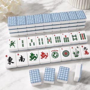 May include: A Mahjong set with white tiles featuring various symbols, numbers, and Chinese characters. The tiles have blue and white checkered tops. The set includes tiles with green and red dragon designs.