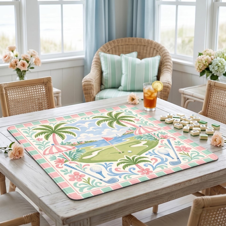 May include: A square golf-themed table mat with a pastel color scheme. The mat features a golf course scene with palm trees, umbrellas, and golf clubs. The border has a pink and green tile design. A glass of iced tea and mahjong tiles are on the table.