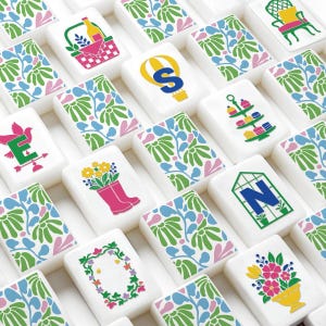 May include: A collection of white rectangular mahjong tiles featuring colorful illustrations including a hot air balloon with the letter S, a picnic basket, a tiered dessert stand, a letter E on a weather vane, and floral patterns.
