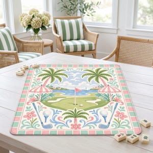 May include: A rectangular golf-themed mat with a pastel color scheme. The design features a golf course scene with palm trees, umbrellas, golf balls, and clubs. The border has alternating pink and green squares. The mat is on a white table.