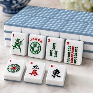 May include: A Mahjong set with white tiles and blue gingham patterned tops. The tiles display numbers, symbols, and Chinese characters in green and red. The set includes a "JOKER" tile.