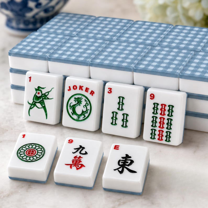 May include: A Mahjong set with white tiles and blue gingham patterned tops. The tiles display numbers, symbols, and Chinese characters in green and red. The set includes a "JOKER" tile.