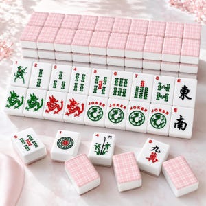 May include: A Mahjong set with white tiles displaying numbers, symbols, and Chinese characters. The tiles are arranged on a surface, some stacked and others displayed. The tops of the tiles have a pink plaid pattern.