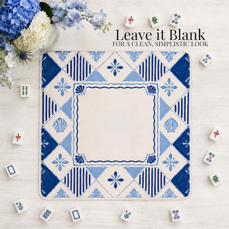 Op de afbeelding: Een vierkante placemat met een blauw en wit tegelontwerp en een centrale lege ruimte. Het patroon bevat geometrische vormen, bloemmotieven en schelpmotieven. De tekst "Leave it Blank" is zichtbaar. Mahjong-tegels zijn verspreid.