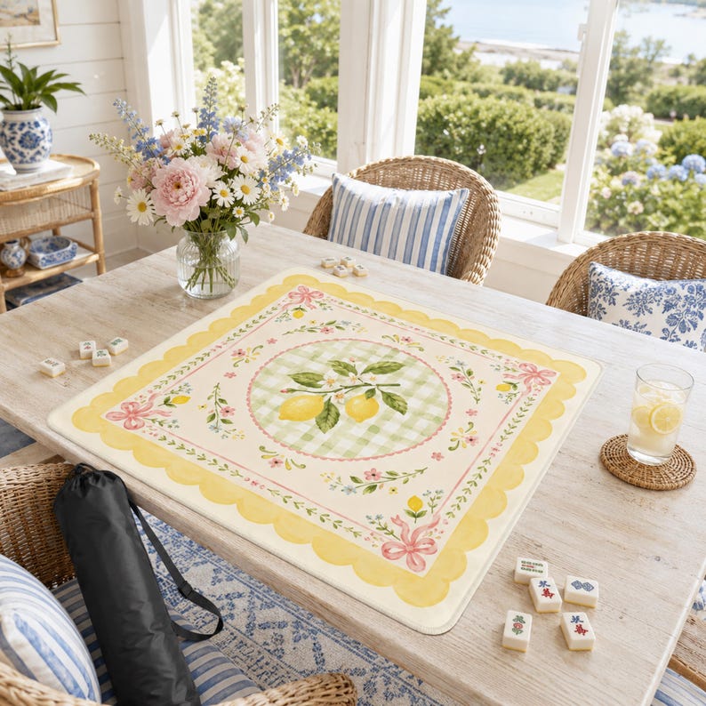 Pode incluir: Um tapete de jogo quadrado creme com uma borda ondulada amarela e um design com tema de lim&atilde;o. O centro apresenta um padr&atilde;o xadrez verde e branco com uma ilustra&ccedil;&atilde;o de ramo de lim&atilde;o. La&ccedil;os rosa e detalhes florais decoram o tapete. Pe&ccedil;as de mahjong espalhadas.
