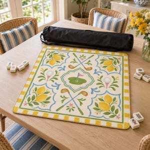 May include: A decorative golf-themed mat with a lemon and floral design. The mat features golf clubs, golf balls, and a green with a flag. A black carrying case and Mahjong tiles are also visible.