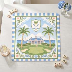 May include: Square golf-themed placemat with a blue and white striped border. The center features a golf course scene with palm trees, a clubhouse, and a shield emblem. The color palette includes shades of blue, green, and beige.